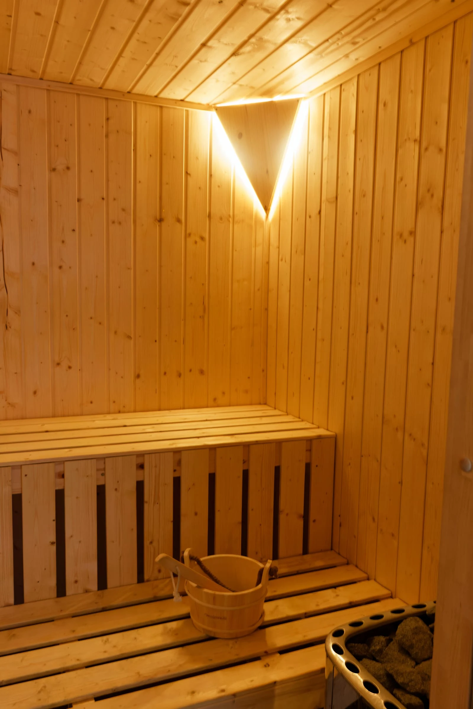 Holzbank, Saunaofen und Aufgusseimer im Innenraum der privaten Sauna